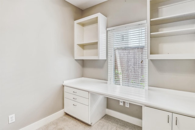 unfurnished office with built in desk, baseboards, and light carpet