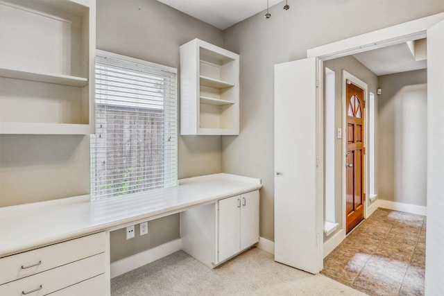 unfurnished office featuring built in desk, baseboards, and light carpet