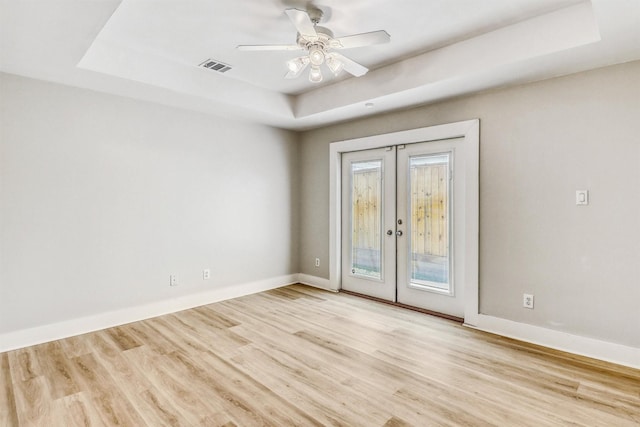 unfurnished room with a raised ceiling, french doors, wood finished floors, and a ceiling fan