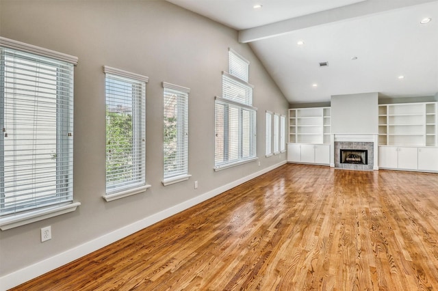 unfurnished living room featuring baseboards, beamed ceiling, a fireplace, wood finished floors, and built in shelves