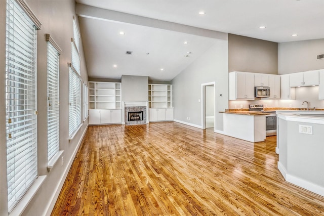 unfurnished living room with high vaulted ceiling, a fireplace, baseboards, light wood finished floors, and a sink