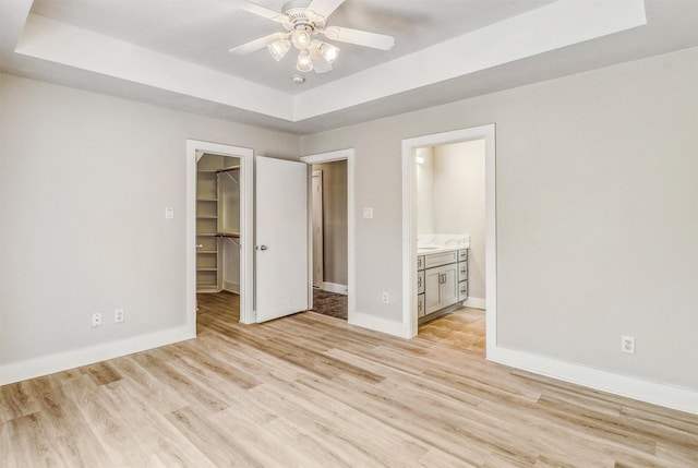 unfurnished bedroom featuring a walk in closet, a tray ceiling, light wood finished floors, baseboards, and a closet
