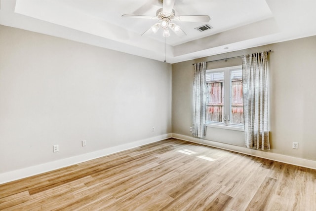 empty room featuring a raised ceiling, light wood finished floors, baseboards, and ceiling fan