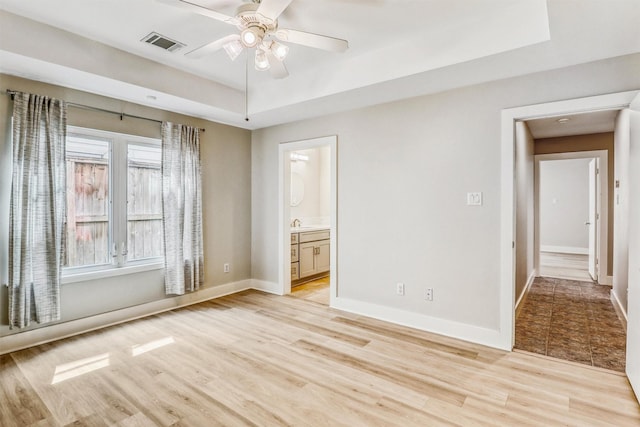 unfurnished room featuring a ceiling fan, light wood-style floors, baseboards, and a raised ceiling