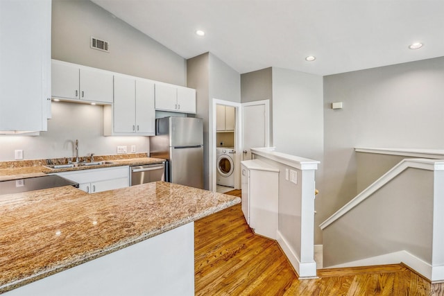 kitchen featuring washer / dryer, a sink, stainless steel appliances, light wood finished floors, and white cabinetry