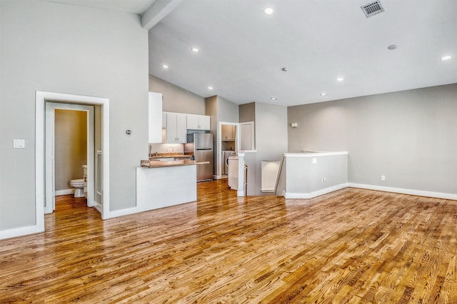 unfurnished living room featuring light wood-style flooring, beam ceiling, recessed lighting, high vaulted ceiling, and baseboards