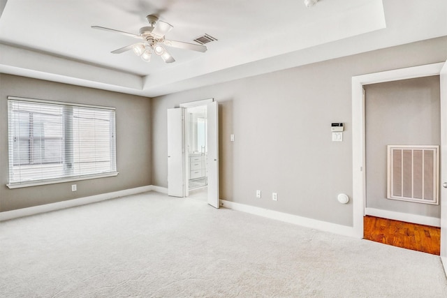 unfurnished bedroom featuring a raised ceiling, carpet flooring, baseboards, ensuite bathroom, and ceiling fan