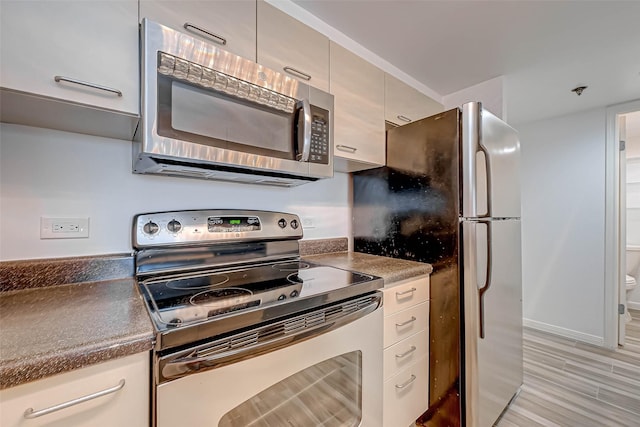 kitchen featuring stainless steel appliances, dark countertops, and light wood-style flooring
