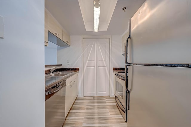 kitchen featuring appliances with stainless steel finishes, a sink, light wood-style flooring, dark countertops, and white cabinets