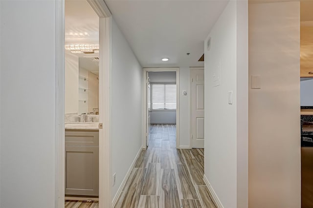 hallway with light wood-style floors, baseboards, a sink, and recessed lighting