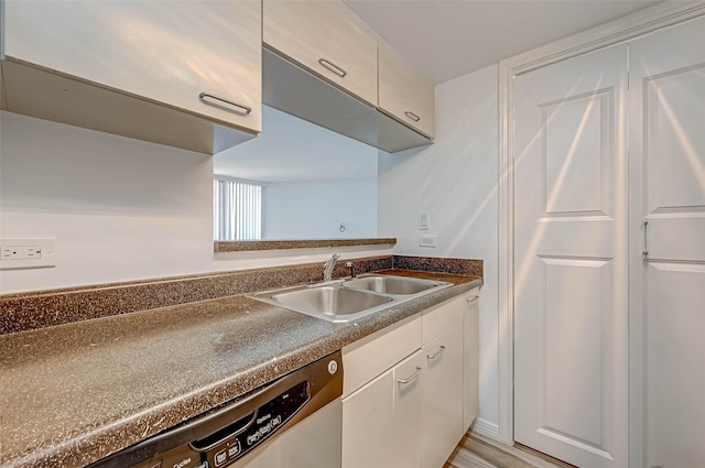 kitchen with a sink, dishwasher, white cabinets, and dark countertops