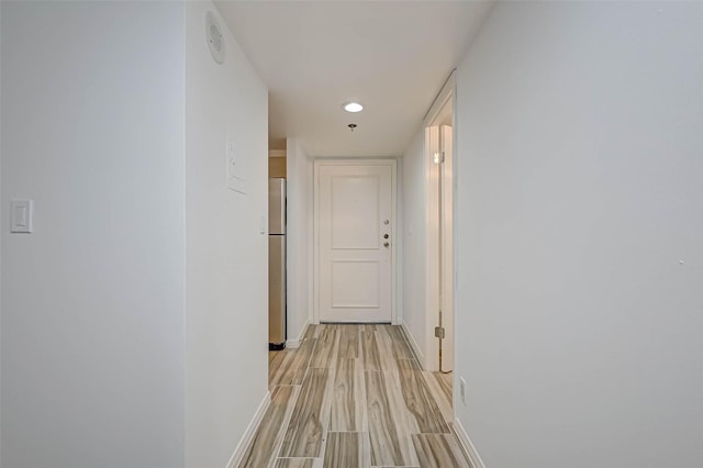 hallway featuring baseboards, light wood-type flooring, and recessed lighting
