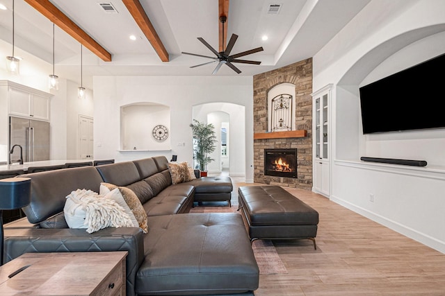 1703 Madera Oaks Ct, Conroe, TX 77304 - living room featuring ceiling fan, arched walkways, light wood finished floors, beamed ceiling, and a stone fireplace