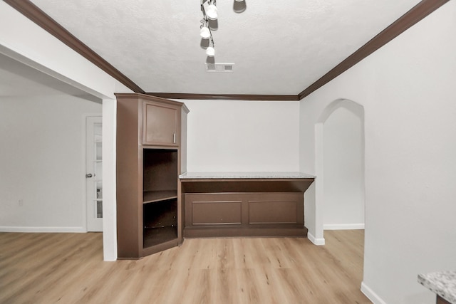 interior space with ornamental molding, arched walkways, light wood-style floors, baseboards, and a textured ceiling