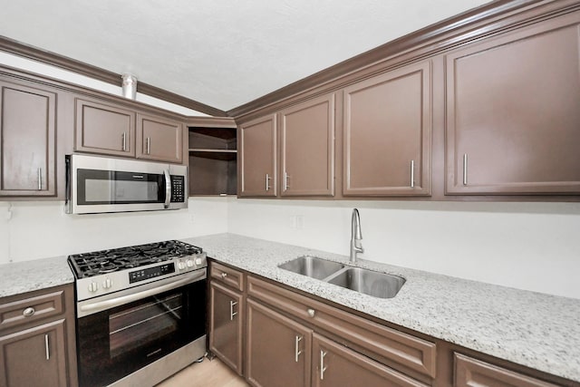 kitchen with stainless steel appliances, a sink, open shelves, light stone countertops, and dark brown cabinetry
