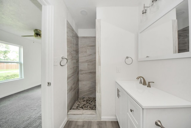 full bathroom with a tile shower, vanity, a ceiling fan, and baseboards