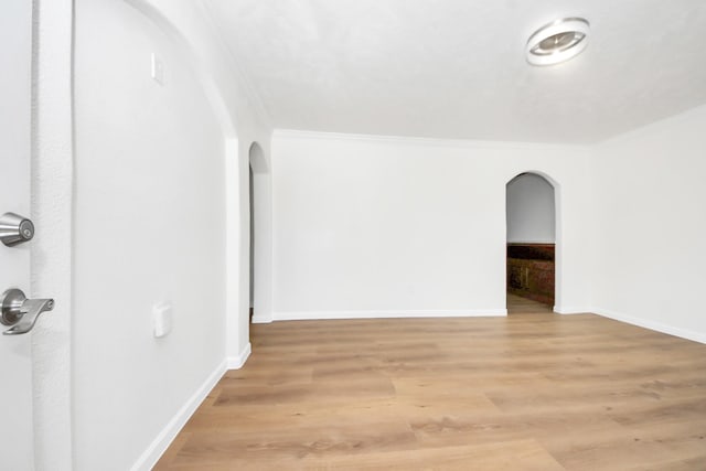 empty room featuring arched walkways, ornamental molding, light wood finished floors, and baseboards