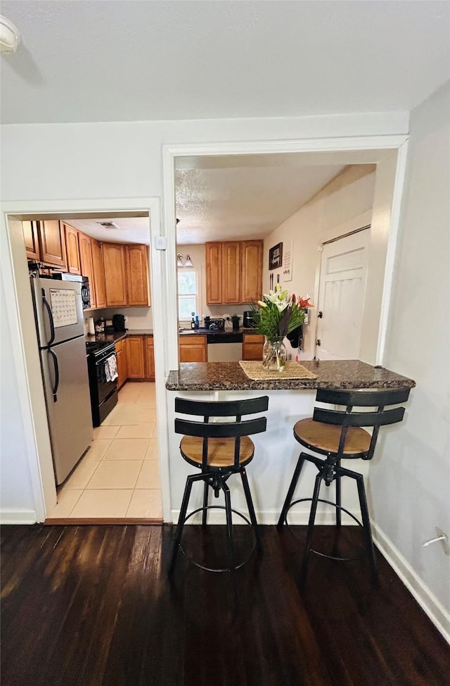 kitchen featuring freestanding refrigerator, black range, brown cabinets, and dark countertops