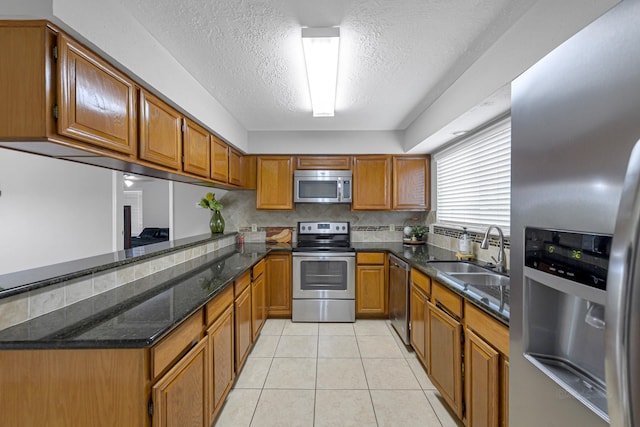 2526 Windswept Dr, Richmond, TX 77406 - kitchen featuring appliances with stainless steel finishes, a sink, brown cabinets, a textured ceiling, and light tile patterned floors