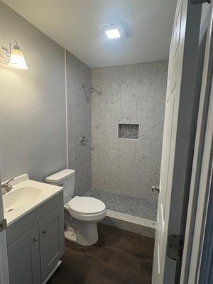 6240 25th St, Groves, TX 77619 - bathroom with wood finished floors, a stall shower, vanity, and toilet