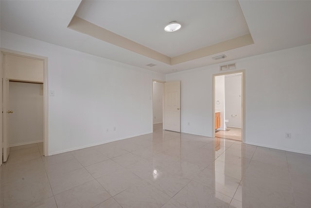 unfurnished bedroom with a tray ceiling, a walk in closet, baseboards, and connected bathroom