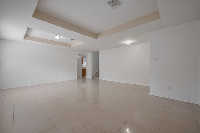 spare room featuring arched walkways, a raised ceiling, light tile patterned flooring, and baseboards