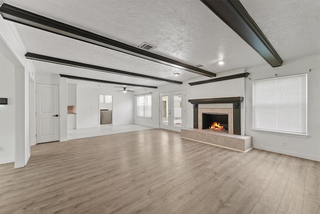 563 Roanoke Dr, Conroe, TX 77302 - unfurnished living room with a textured ceiling, beamed ceiling, light wood-style flooring, baseboards, and a premium fireplace