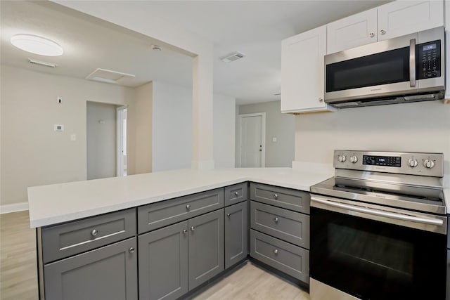 kitchen featuring stainless steel appliances, gray cabinets, a peninsula, light wood finished floors, and light countertops