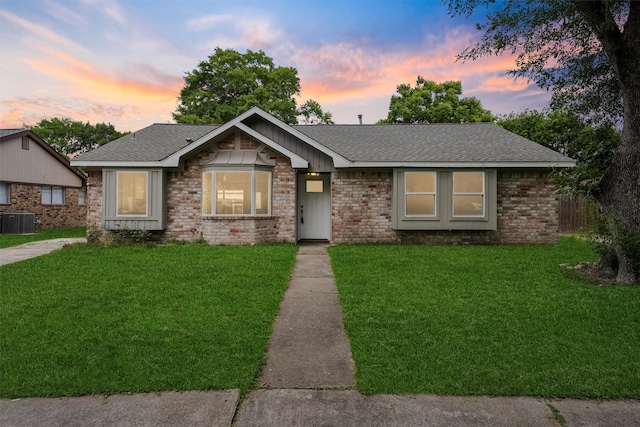 view of front of home with central air condition unit, a lawn, roof with shingles, and brick siding