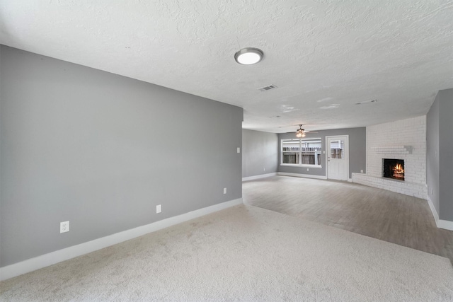 unfurnished living room featuring carpet flooring, a brick fireplace, baseboards, a textured ceiling, and a ceiling fan
