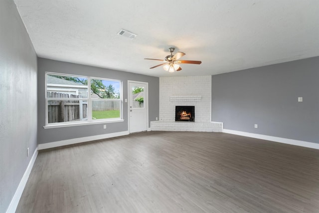 unfurnished living room with a ceiling fan, wood finished floors, baseboards, and a brick fireplace