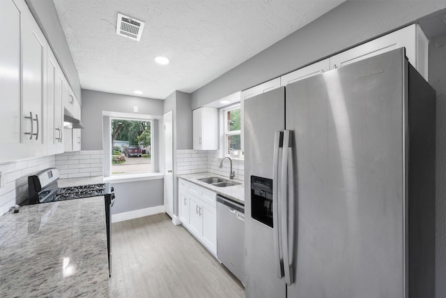 kitchen featuring stainless steel appliances, a sink, light wood finished floors, white cabinets, and light stone countertops