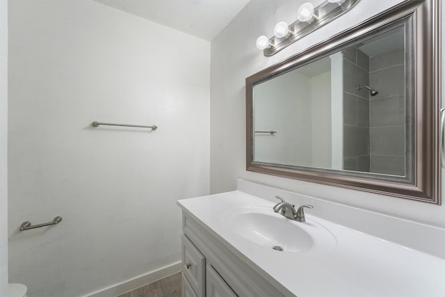 full bath featuring vanity, wood finished floors, baseboards, and a shower