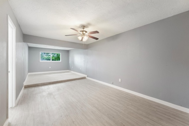 empty room with a ceiling fan, light wood-style floors, a textured ceiling, and baseboards