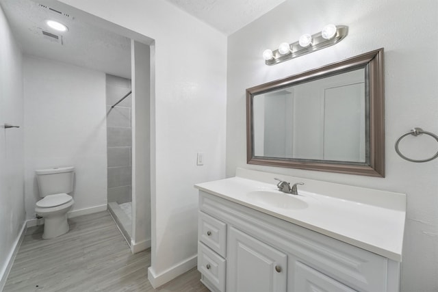 full bath featuring toilet, baseboards, vanity, tiled shower, and wood finished floors