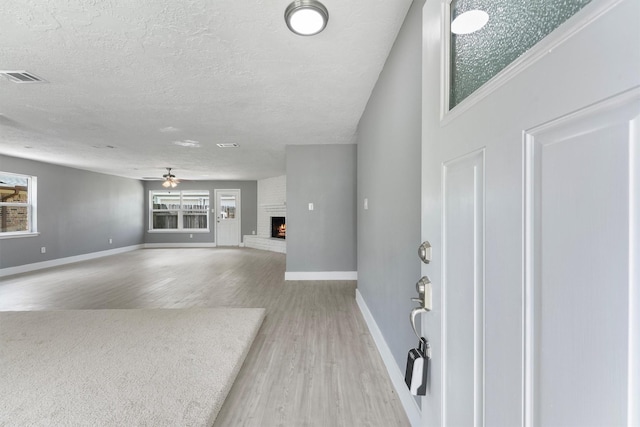 unfurnished living room featuring wood finished floors, a ceiling fan, a brick fireplace, a textured ceiling, and baseboards