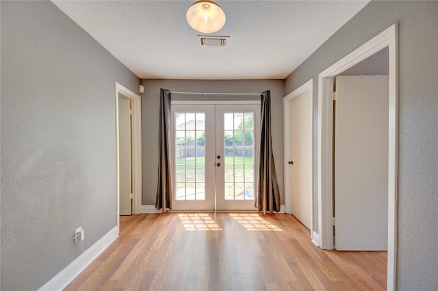 entryway with french doors, light wood finished floors, baseboards, and a textured wall