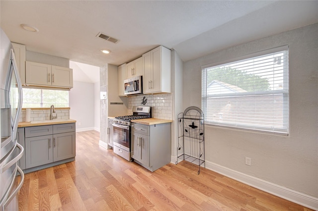 kitchen with stainless steel appliances, gray cabinetry, tasteful backsplash, and light wood-style flooring
