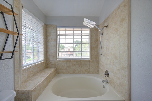 bathroom featuring toilet, a textured wall, and shower / tub combination