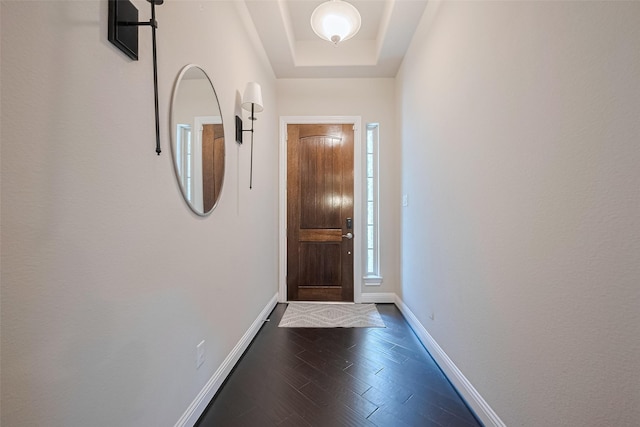 doorway to outside featuring a tray ceiling, baseboards, and dark wood-style floors