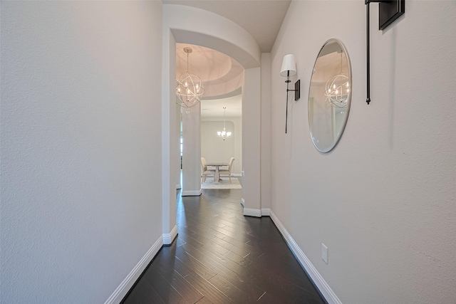 corridor featuring a chandelier, baseboards, dark wood-style floors, and arched walkways