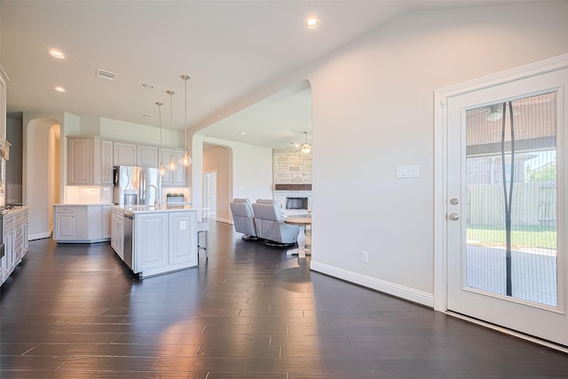 kitchen with open floor plan, a kitchen island with sink, arched walkways, light countertops, and dark wood finished floors