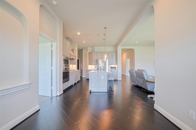 kitchen featuring stainless steel appliances, light countertops, a kitchen island with sink, open floor plan, and dark wood-style floors