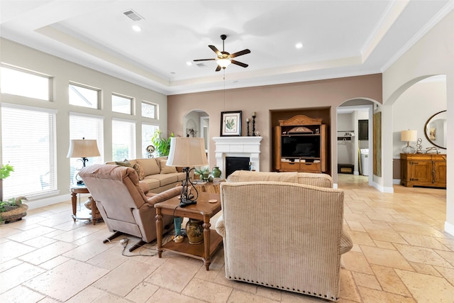 222 Reynosa Ct, Pinehurst, TX 77362 - living room with a tray ceiling, stone tile flooring, a ceiling fan, crown molding, and a fireplace