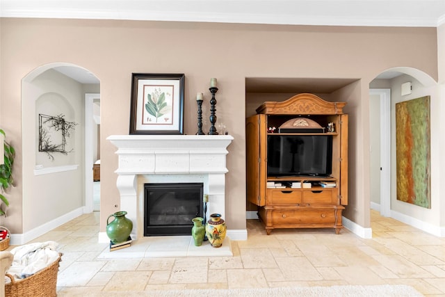 222 Reynosa Ct, Pinehurst, TX 77362 - living area featuring stone tile floors, a glass covered fireplace, baseboards, crown molding, and arched walkways