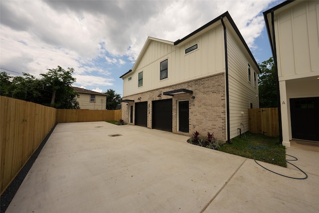 back of property with brick siding, board and batten siding, a garage, and fence