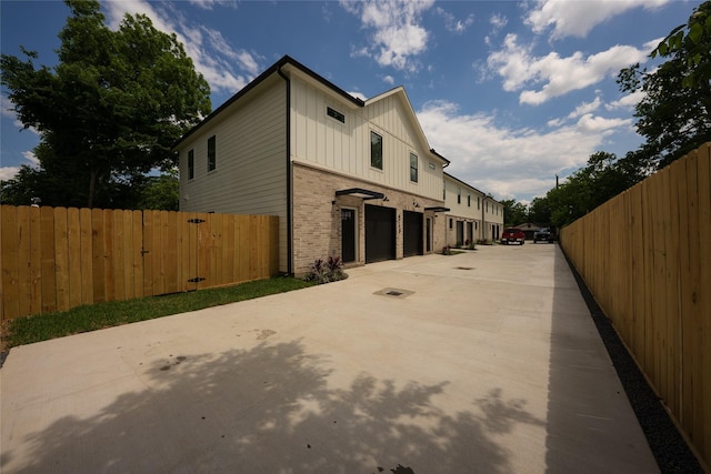 view of property exterior with board and batten siding, driveway, brick siding, and fence