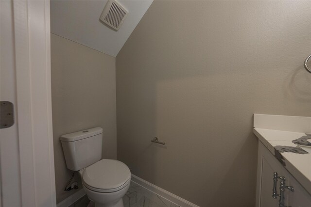 half bathroom featuring marble look tile flooring, toilet, vanity, baseboards, and vaulted ceiling