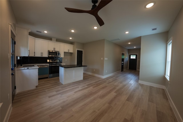 kitchen featuring appliances with stainless steel finishes, open floor plan, white cabinets, decorative backsplash, and a ceiling fan