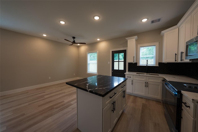 kitchen with black electric range oven, a sink, light wood-type flooring, white cabinets, and decorative backsplash